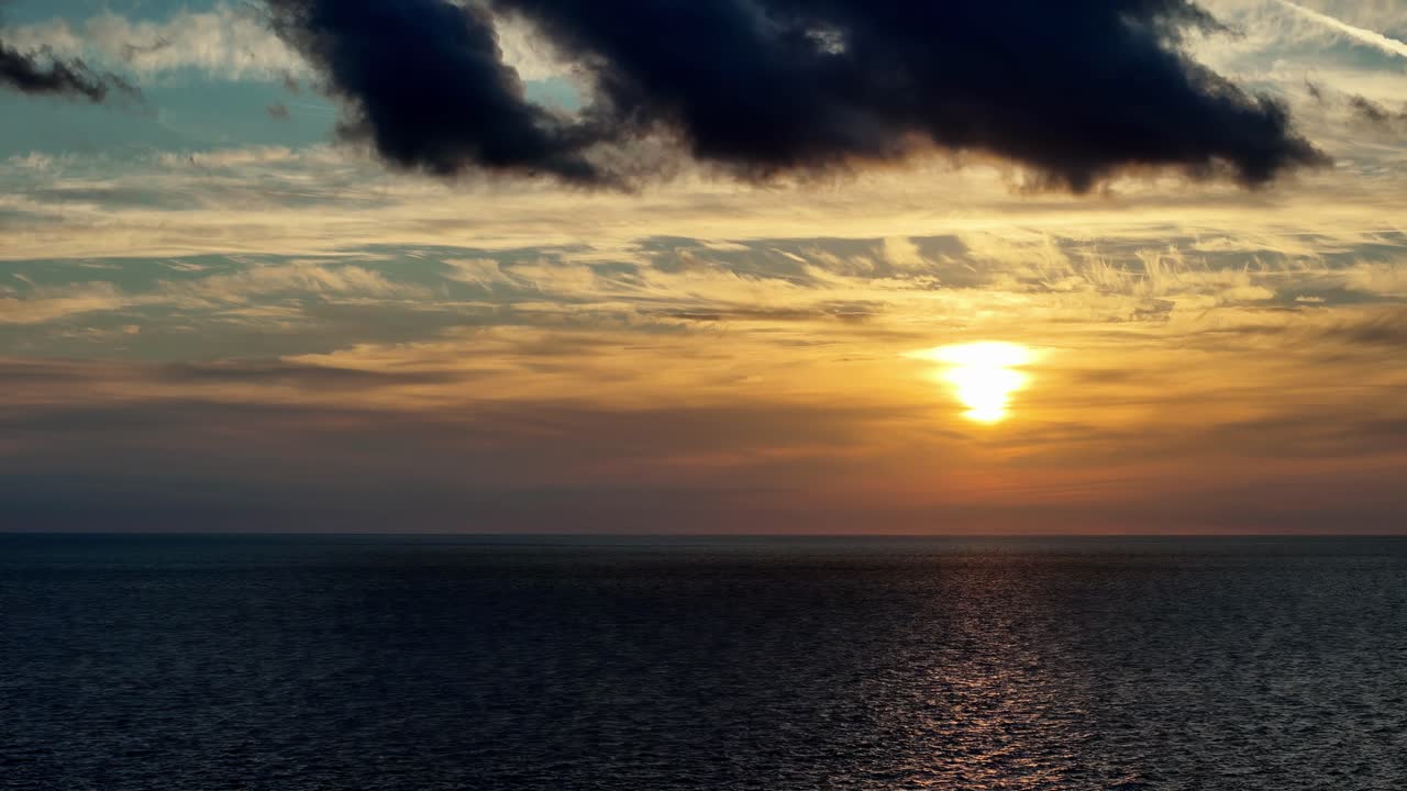 Dramatischer goldener Sonnenuntergang über dem Mittelmeer in der Nähe von Gozo und Comino mit markanten dunklen Wolken und strahlenden orangefarbenen Horizonten, aufgenommen aus einem weiten Küsten-Winkel während der warmen Sommerzeit