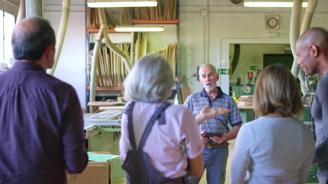 Experienced Craftsman Discussing Project with Group of Apprentices in Workshop