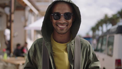 portrait of handsome hispanic man smiling happy on sunny beachfront wearing hoodie