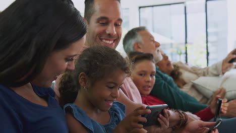 Multi-Generation-Family-On-Sofa-Watching-TV-And-Playing-With-Digital-Tablet-And-Mobile-Phones