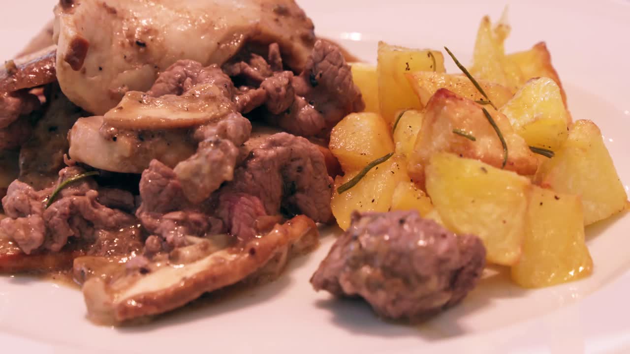 A medium shot pans right, showcasing a plate of tender meat with mushrooms and roasted potatoes, garnished with rosemary, highlighting a rustic, savory dish.
