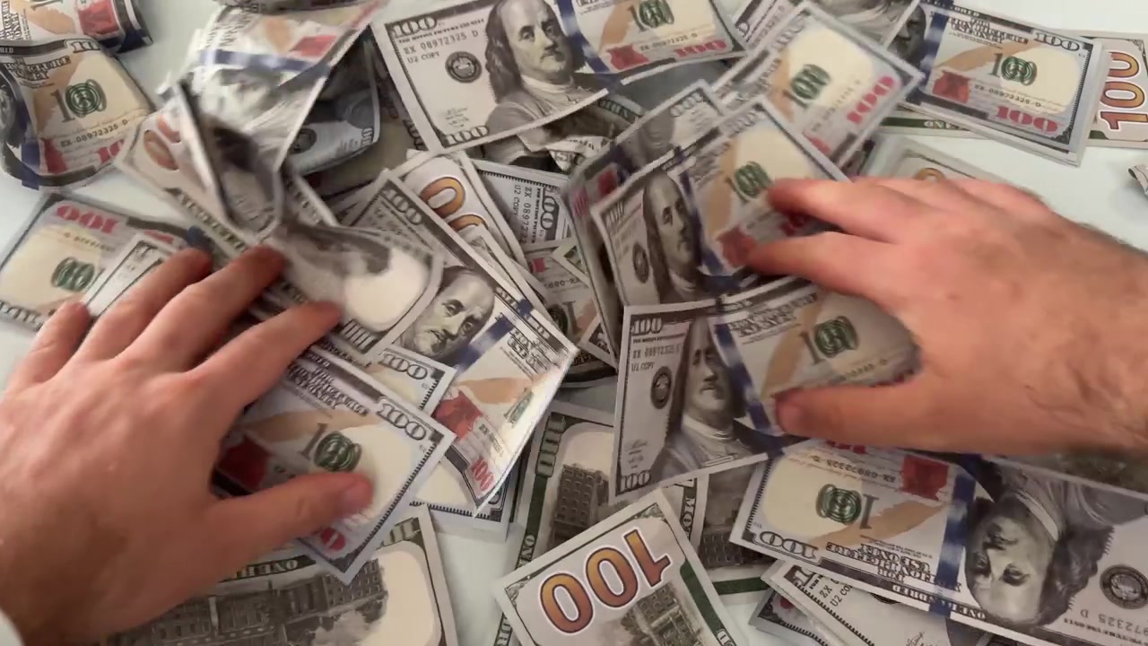 Hender teller en stor haug med amerikanske dollarsedler på et bord