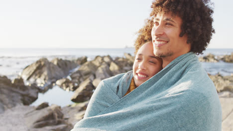 Pareja-Afroamericana-Envuelta-En-Una-Manta-Parada-En-Las-Rocas-Cerca-Del-Mar