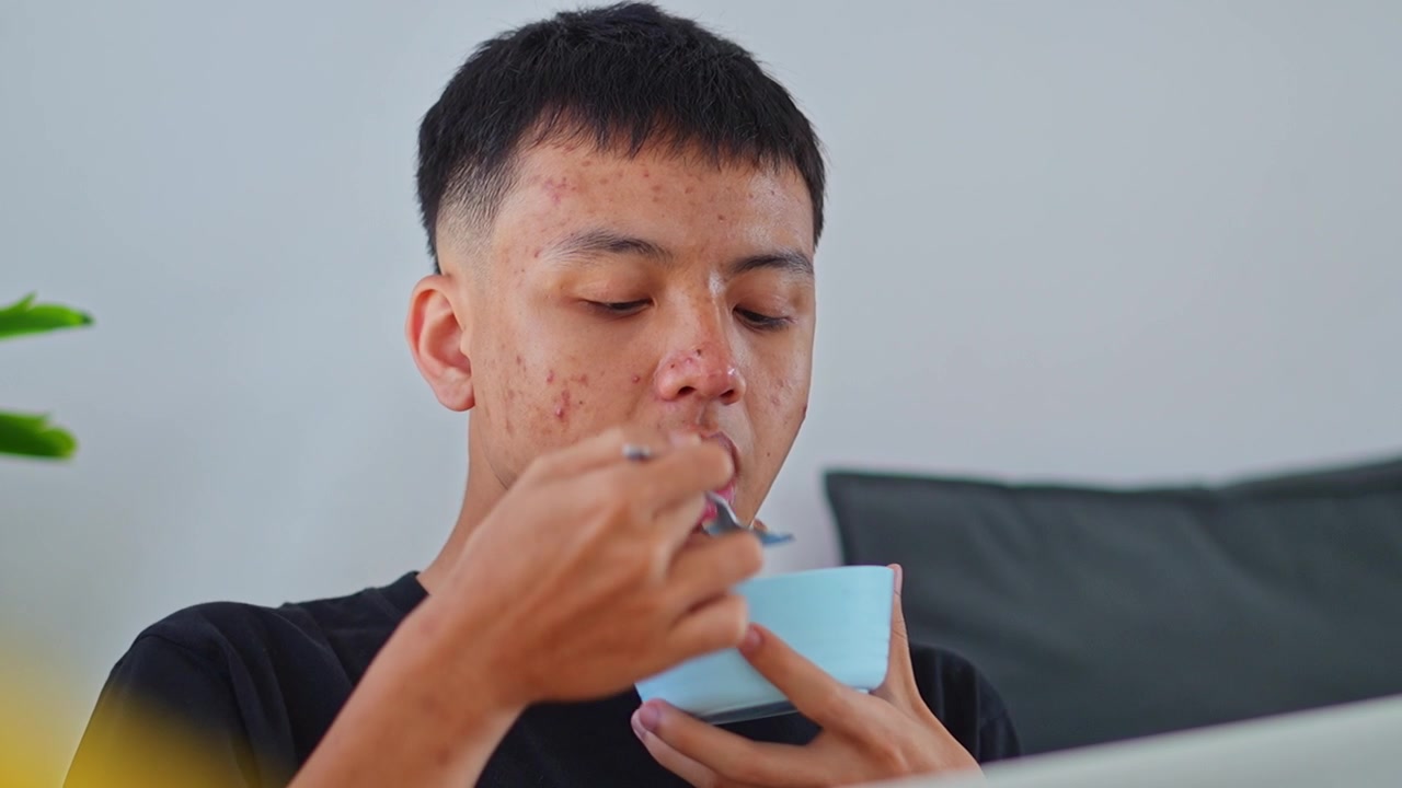 Primo piano di un giovane uomo che mangia cereali con un cucchiaio e beve il latte rimasto direttamente dalla ciotola blu.