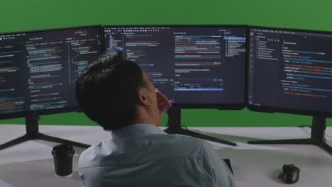 back view of tired asian man developer yawning while write code with multiple computer screens in green screen studio