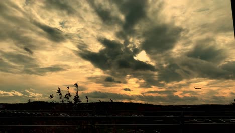 Plane-approaching-landing-at-sunset-against-the-background-of-orange-sun-behind-clouds