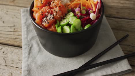 composition of bowl of rice, salmon and vegetables with chopsticks on wooden background