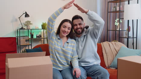 Un-Hombre-Y-Una-Mujer-Jóvenes-De-Familia-Levantan-Las-Manos-Y-Juntan-Los-Brazos-Formando-La-Forma-Del-Techo-De-Una-Casa,-Símbolo-De-Un-Nuevo-Hogar