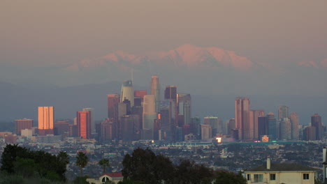 downtown la skyline from kenneth hahn state park at sunset with snowcapped mountains in the background