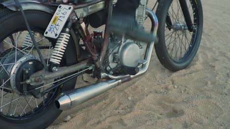 Man-in-tall-black-boots-kick-starts-vintage-retro-chopper-motorcycle-in-the-desert