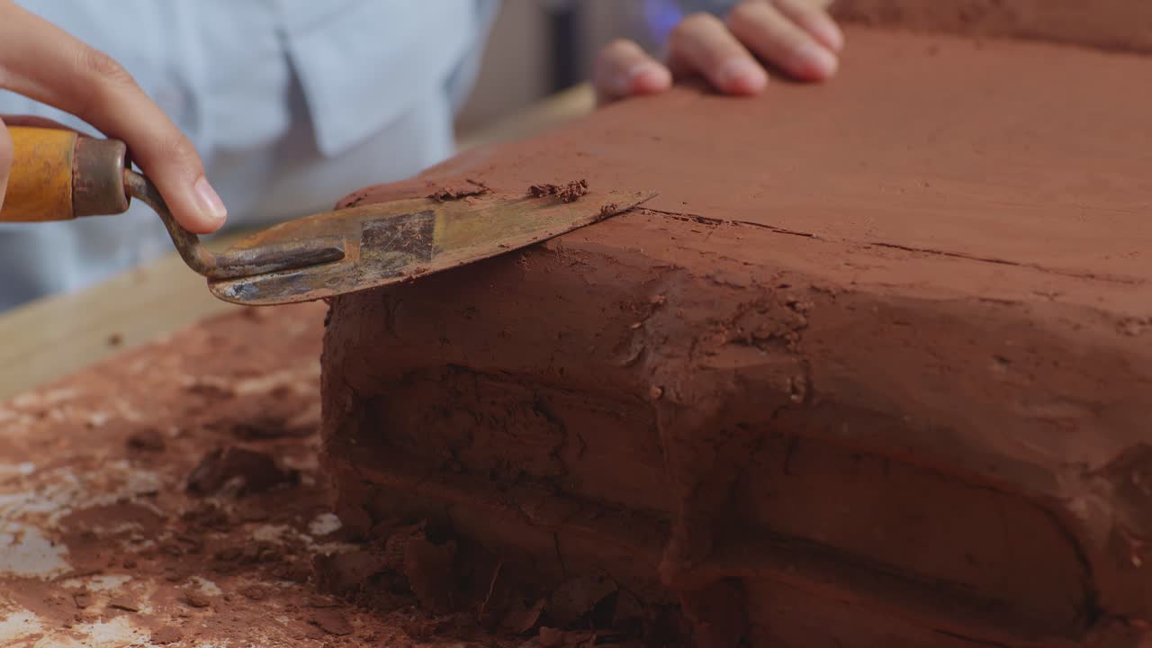 primer plano de las manos de una mujer diseñadora de automóviles usando una espátula para suavizar la superficie y crear detalles en la escultura de arcilla de automóvil en el estudio