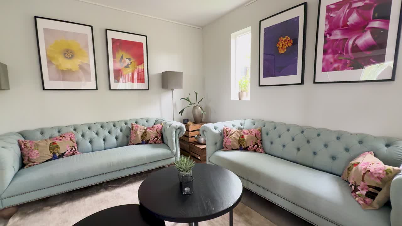 Sala de estar moderna e iluminada com sofás capitonê azul-claro e arte de parede floral colorida
