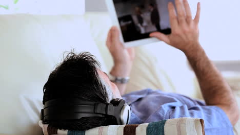 mature man lying on the couch listening to music and using tablet pc