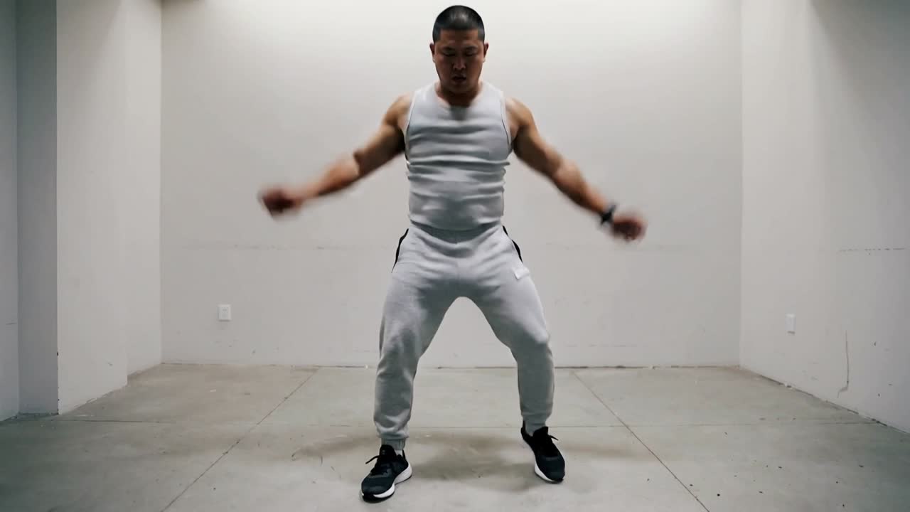 Posa iniziale, uomo asiatico che esegue una routine di esercizi per braccia e gambe, terminando con i pugni vicino ai fianchi in studio, con canotta e joggers.