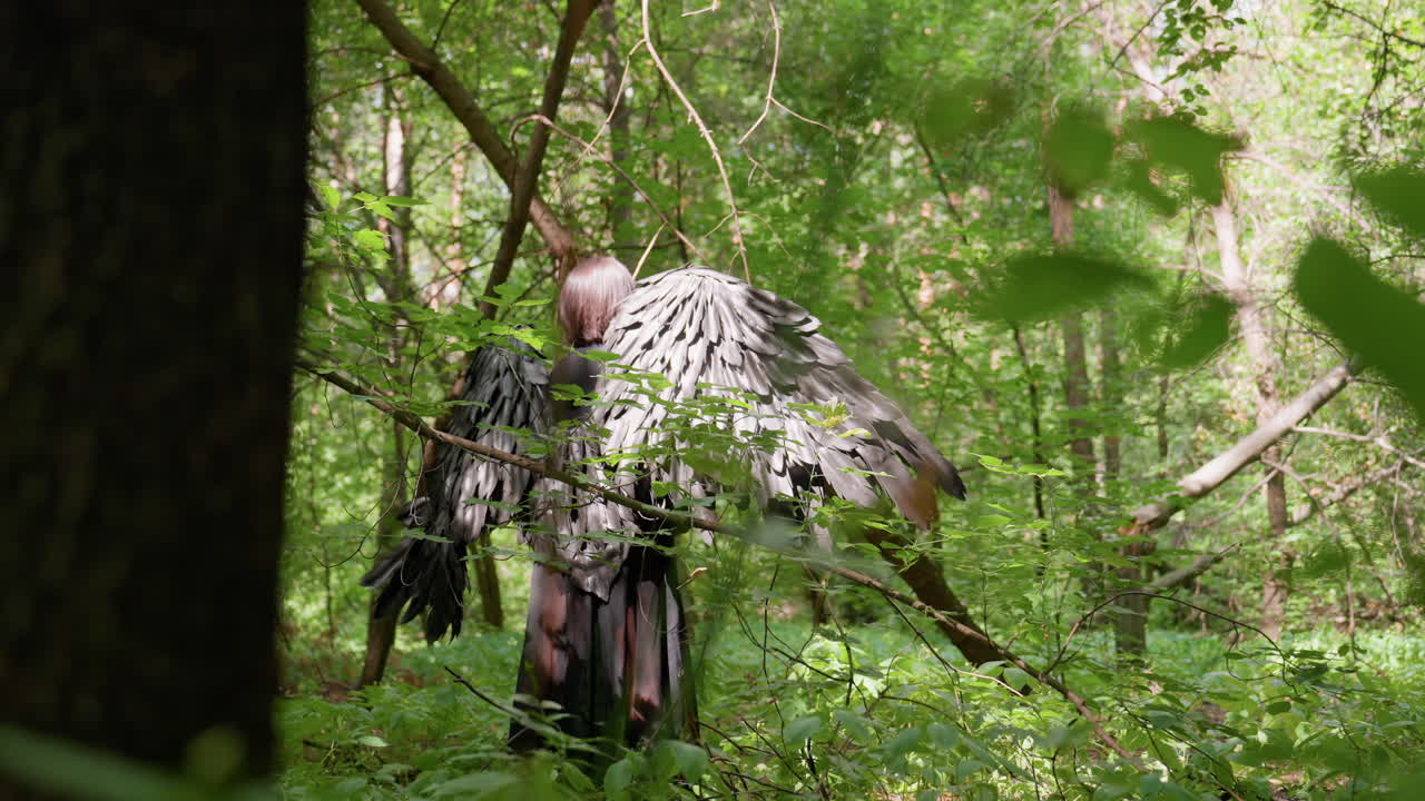 Back view of woman with large black wings standing in lush green forest under sunlight, wings spread slightly among trees and branches, creating mystical serene atmosphere