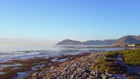 Aerial-look-over-a-rocky-beach-during-golden-hour-with-mountains