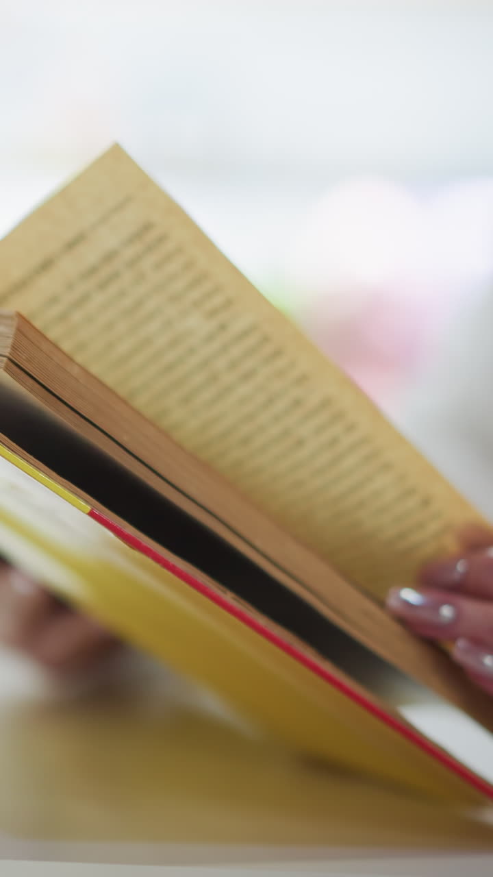 primer plano de manos hojeando las páginas de un libro amarillo abierto en una mesa, con un fondo borroso con una taza de café, creando una atmósfera serena y reflexiva