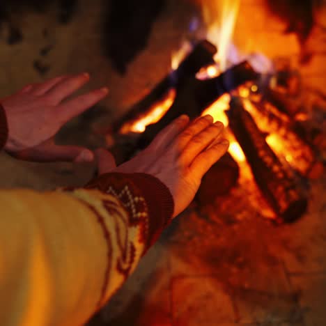 male's hands by warm fireplace. burning fireplace warming cold hands of a man at comfortable home in winter season. close-up.