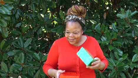 Black-woman-wearing-glasses-excitedly-shakes-gift-boxes-to-determine-gifts-inside