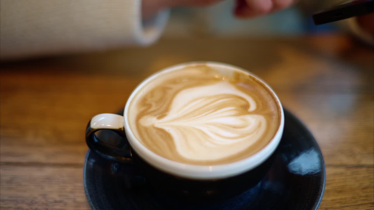 Woman drinking latte coffee while watching content on smartphone