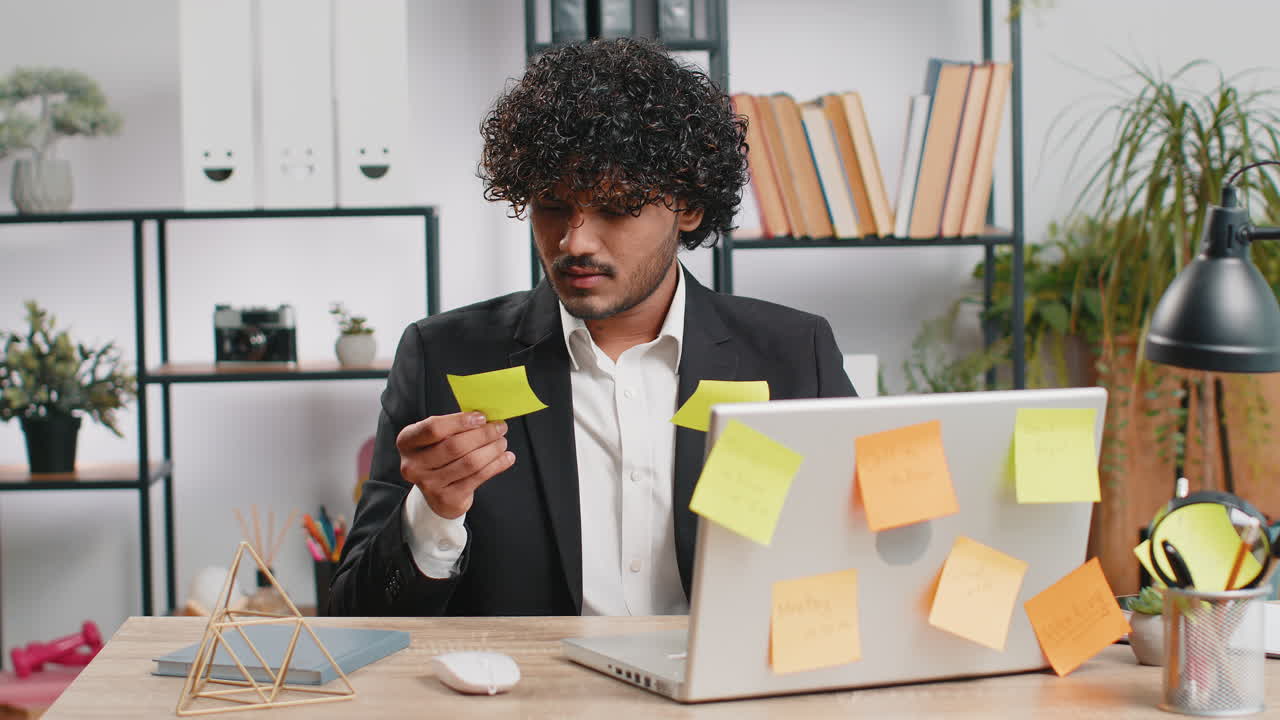 Tired sad exhausted businessman working on laptop at office with many sticker tasks panic attack