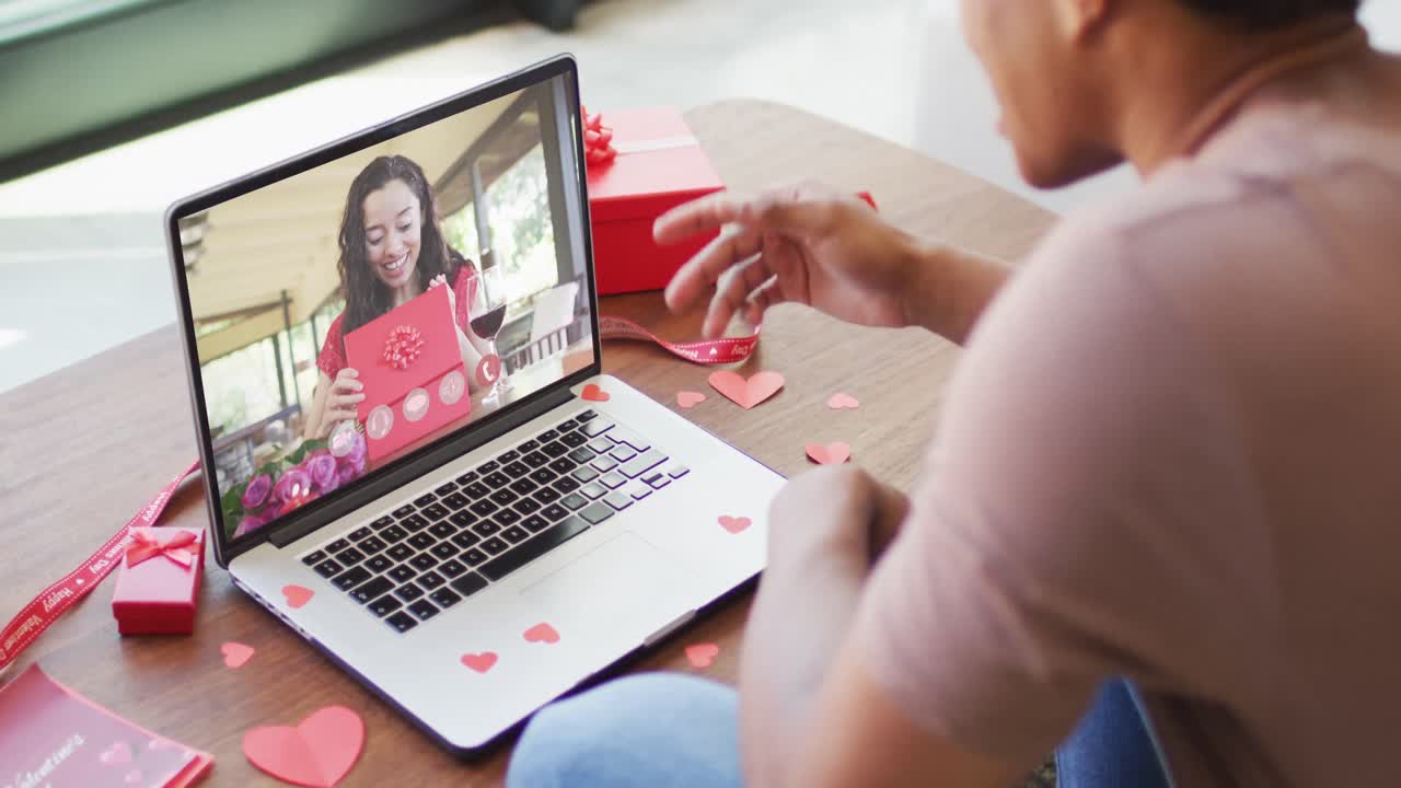 Happy biracial woman with vitiligo opening gift and making valentine's day video call on laptop