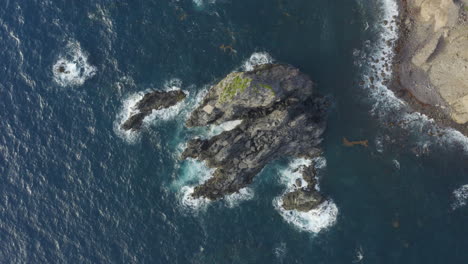 Abandoned Caribbean beach in the early morning. Plan view, smooth fly up and spin above the blue ocean, large centre rock and cliffside.4K UHD at 23.98 fps