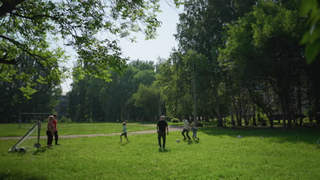 familia disfruta de un juego de fútbol al aire libre en un día soleado como el hijo en blanco dribbles más allá de su hermano en rojo y persigue la pelota, que cruza el poste de la meta