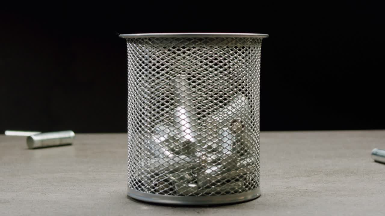 Silver batteries AA and AAA falling into wastebasket close-up. Double-A battery is a standard size single cell cylindrical dry battery. Batteries are common in portable electronic devices. Environmental impacts of lithium-ion batteries concept. An AA battery is composed of a single electrochemical c