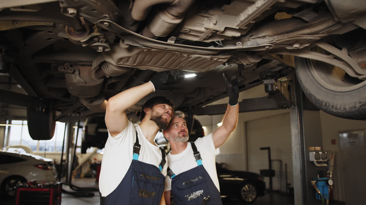 dos mecánicos inspeccionando el tren de aterrizaje de un coche