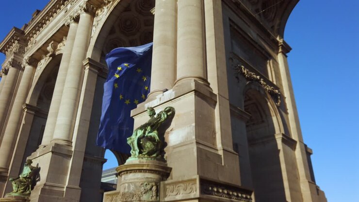 EU flag waving under Cinquantenaire arch with sculpture view