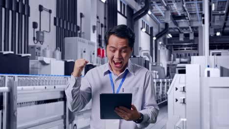 Asian Male Professional Worker Standing With His Tablet With Water Production in Bottling Factory, He Raises His Fist Up With Screaming Goal