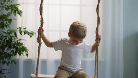 Cute-blond-boy-sits-on-swing-attached-in-children-room