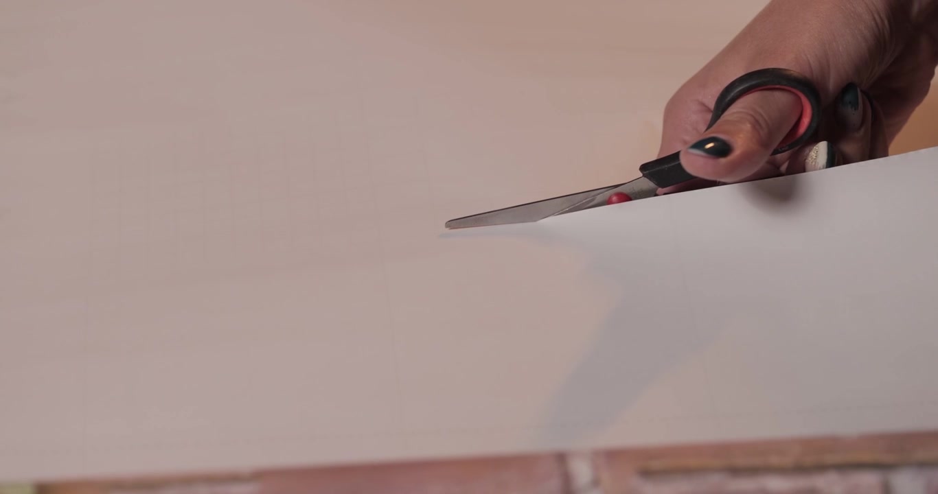 Close-up of young Caucasian woman's hands with black nails cutting self-adhesive wallpaper with scissors, 4K shot