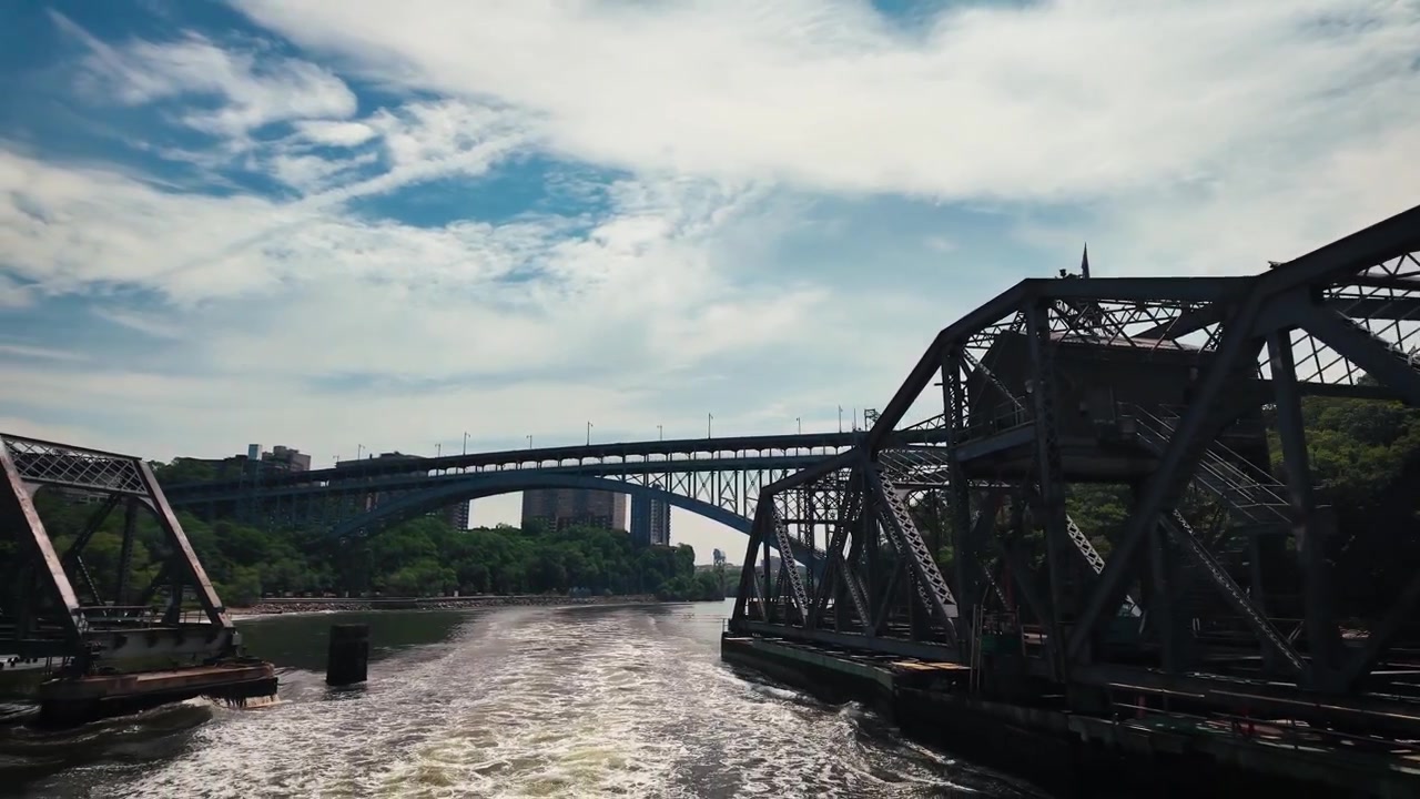 Filmisk agterudsigt fra en bevægende båd, der passerer gennem den historiske Spuyten Duyvil Railroad Swing Bridge med Henry Hudson Bridge, der spænder over Harlem River i det nordlige Manhattan, New York City.