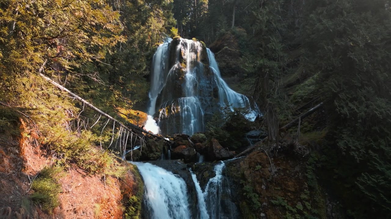 Vista aerea panoramica che si allontana delle cascate superiori e inferiori di Falls Creek Falls alla luce della sera, con il canyon boscoso circondato da superfici rocciose.
