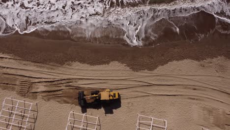 Luftaufnahme-Von-Oben-Nach-Unten-Eines-Baggers,-Der-Sand-Am-Strand-Neben-Wellen-Des-Ozeans-Packt-Und-Transportiert---4k