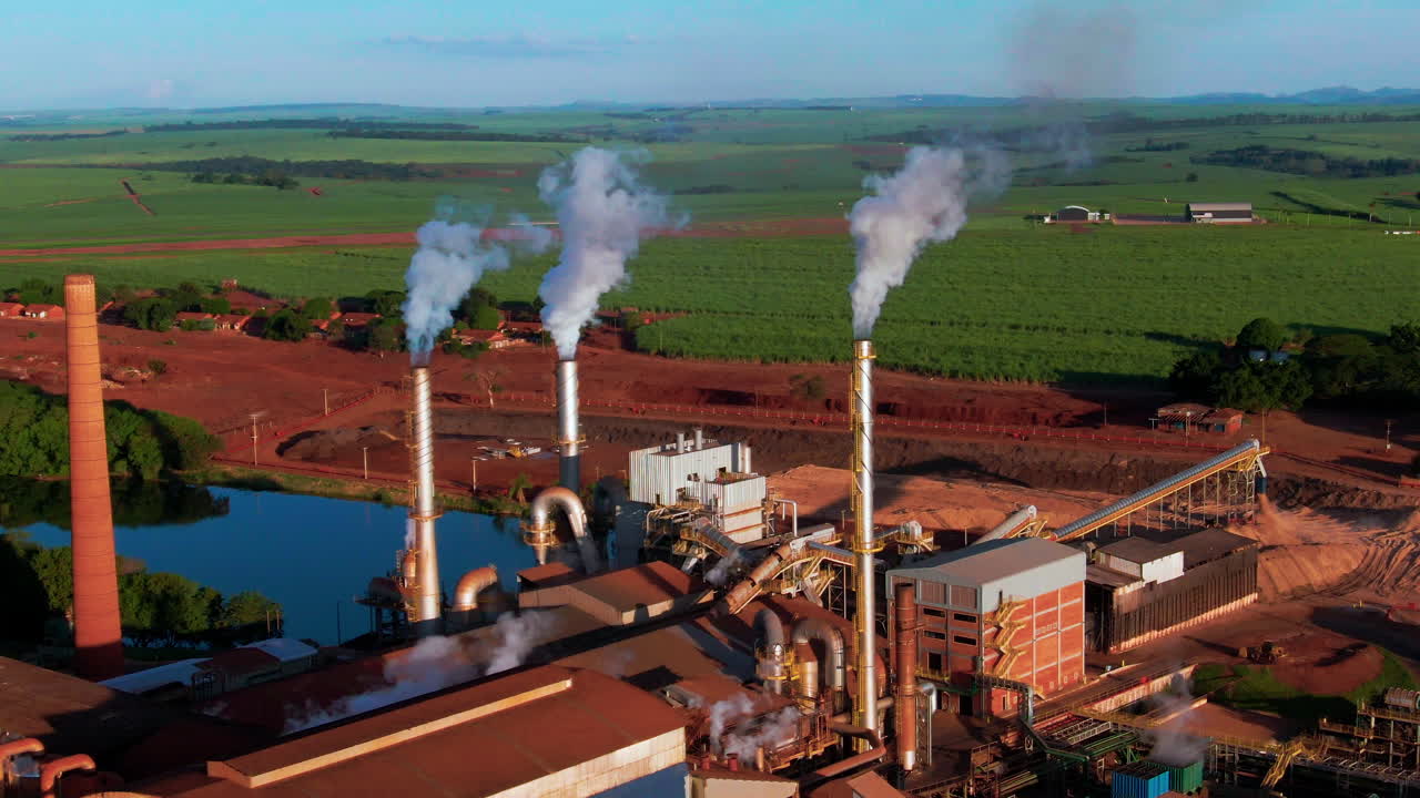 Drone aerial landscape of steam coming from turbines at Ethanol production plant factory with warehouse facility in farmland countryside region valley of Brazil South America industry processing