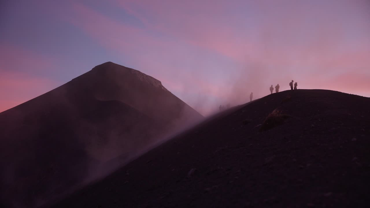 la gente en la cresta del volcán de fuego es golpeada por el polvo y los fuertes vientos durante la impresionante puesta de sol con nubes rosadas, guatemala