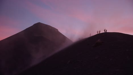 people on ridge of fuego volcano get hit by dust and strong winds during breathtaking sunset with pink clouds, guatemala