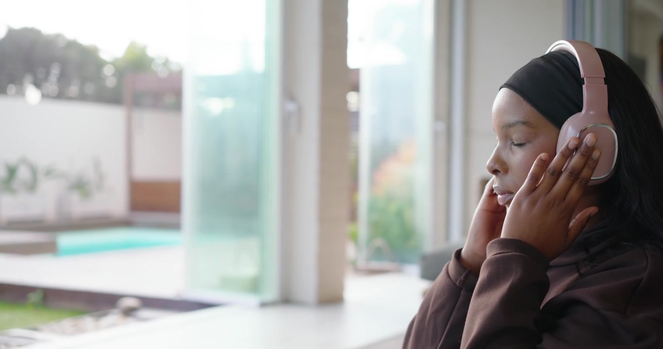 Donna afroamericana che scorre il telefono regolando le cuffie, cercando calma su un sedile vicino alla porta, con spazio per il testo.