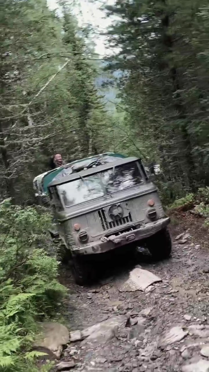 Robusto camion fuoristrada sale una ripida pista rocciosa attraverso una fitta foresta sulla strada per i laghi Karakol, Monti Altai, Repubblica dell'Altai, Russia.