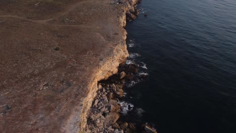 Drone-top-down-aerial-view-of-waves-splash-against-rocky-seashore,-background