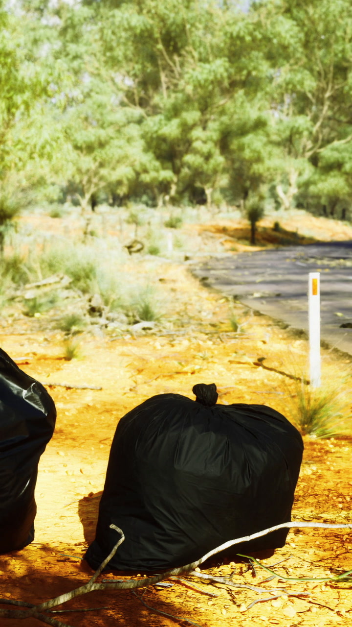 Garbage bags placed near a dirt road in a natural landscape during daytime