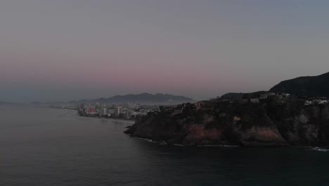 Panorámica-Aérea-Que-Revela-El-Vasto-Barrio-De-Barra-Da-Tijuca-En-Río-De-Janeiro-Con-Niebla-Matutina-Detrás-De-Los-Acantilados-De-La-Playa-De-Joatinga.