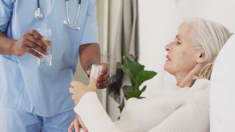 Video-of-midsection-of-african-american-male-doctor-giving-water-to-caucasian-senior-woman