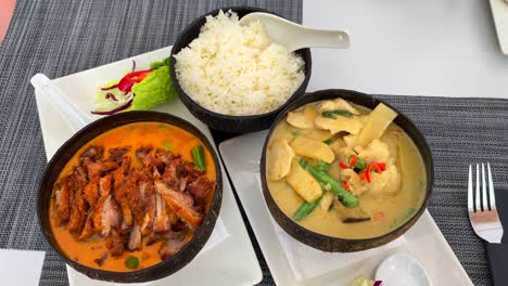 crispy duck in red curry sauce with rice and spicy thai coconut soup with chicken and vegetables in a coconut bowl, thai cuisine restaurant, 4k shot