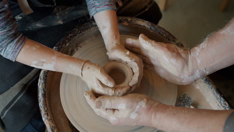 child and adult shaping clay on pottery wheel