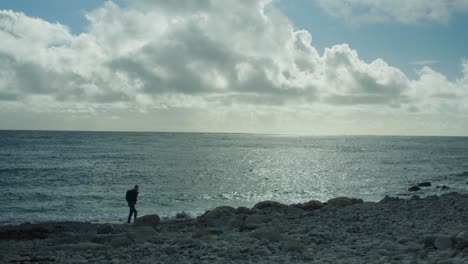toma de paisaje panorámico en cámara lenta de 4k de un hombre caminando en la playa rocosa de la iglesia ope, en la isla de portland, en dorset, inglaterra, en un día soleado