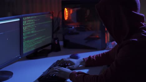side view of hacker sitting near computer monitors with green code screens.